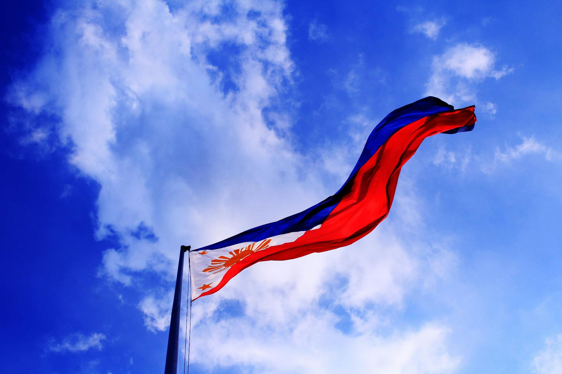 Philippine flag waving in the sky with clouds, representing the vibrant Bisaya culture in America and the importance of accurate English to Visayan translation