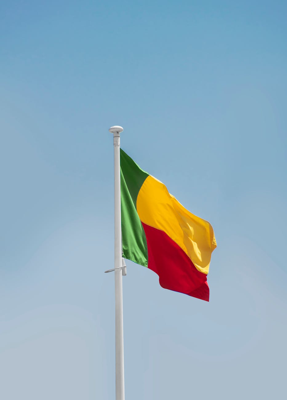 Benin National Flag hanging on a white pole against a backdrop of clear blue sky