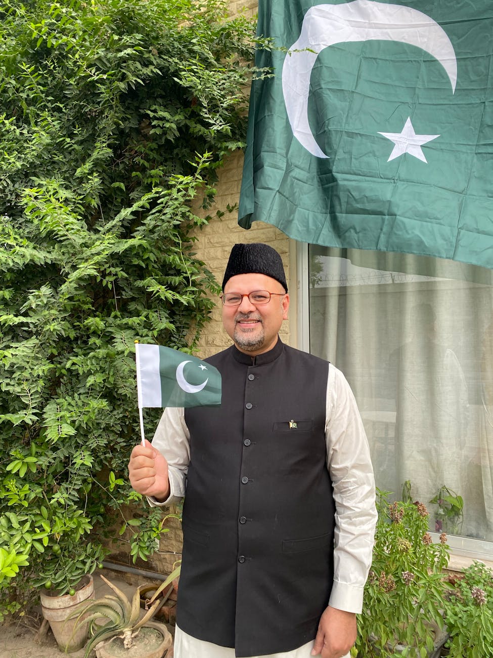 A man in traditional Pakistani attire proudly holding the Pakistan flag, representing the Mirpuri community's cultural pride and connection to their roots.