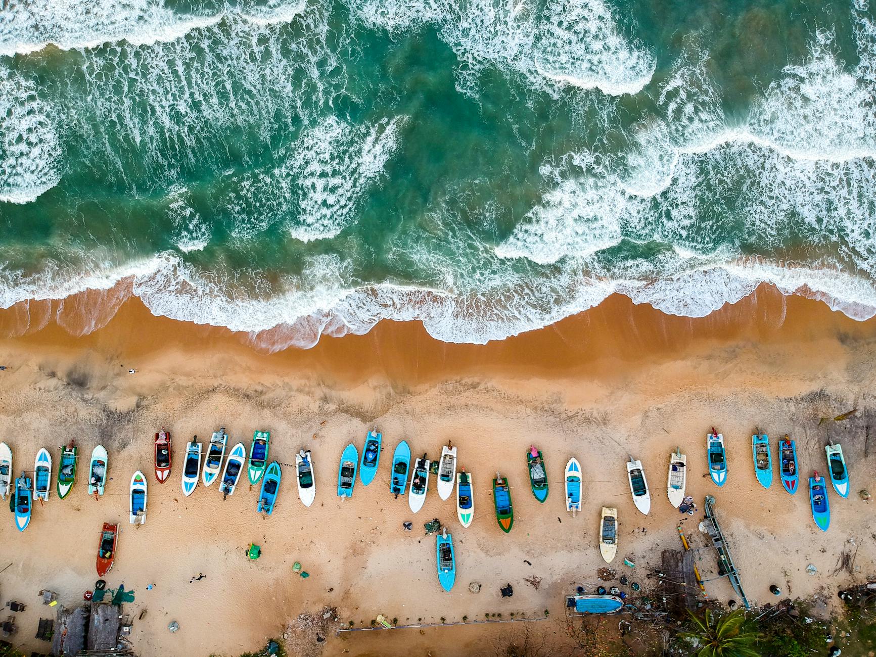 Aerial view of colorful boats on a sandy Sri Lankan beach, highlighting the island's connection to the ocean and the Sinhala language to English translation services enabling global communication.