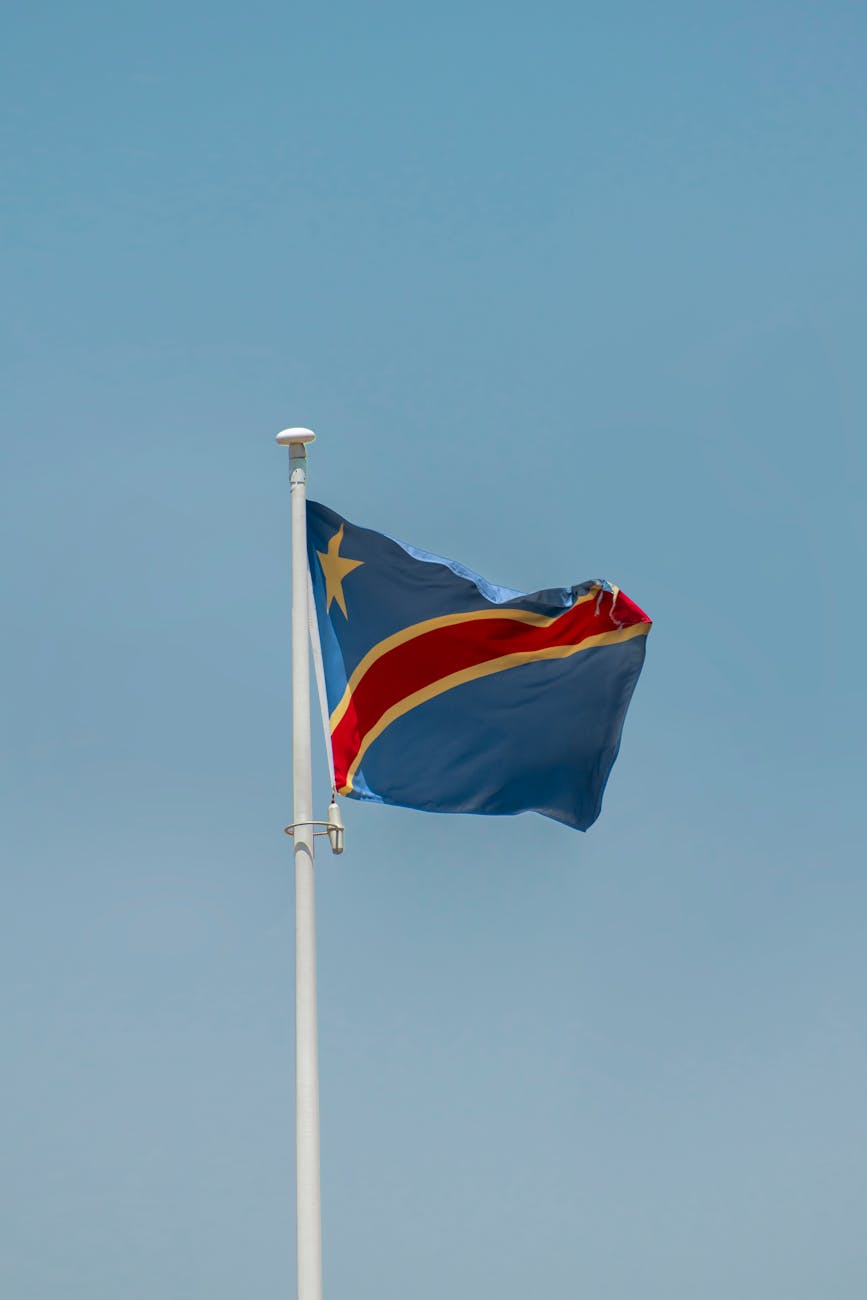 The flag of the Democratic Republic of Congo flying against a clear blue sky, symbolizing the homeland of the Banyamulenge people and their language, Kinyamulenge.