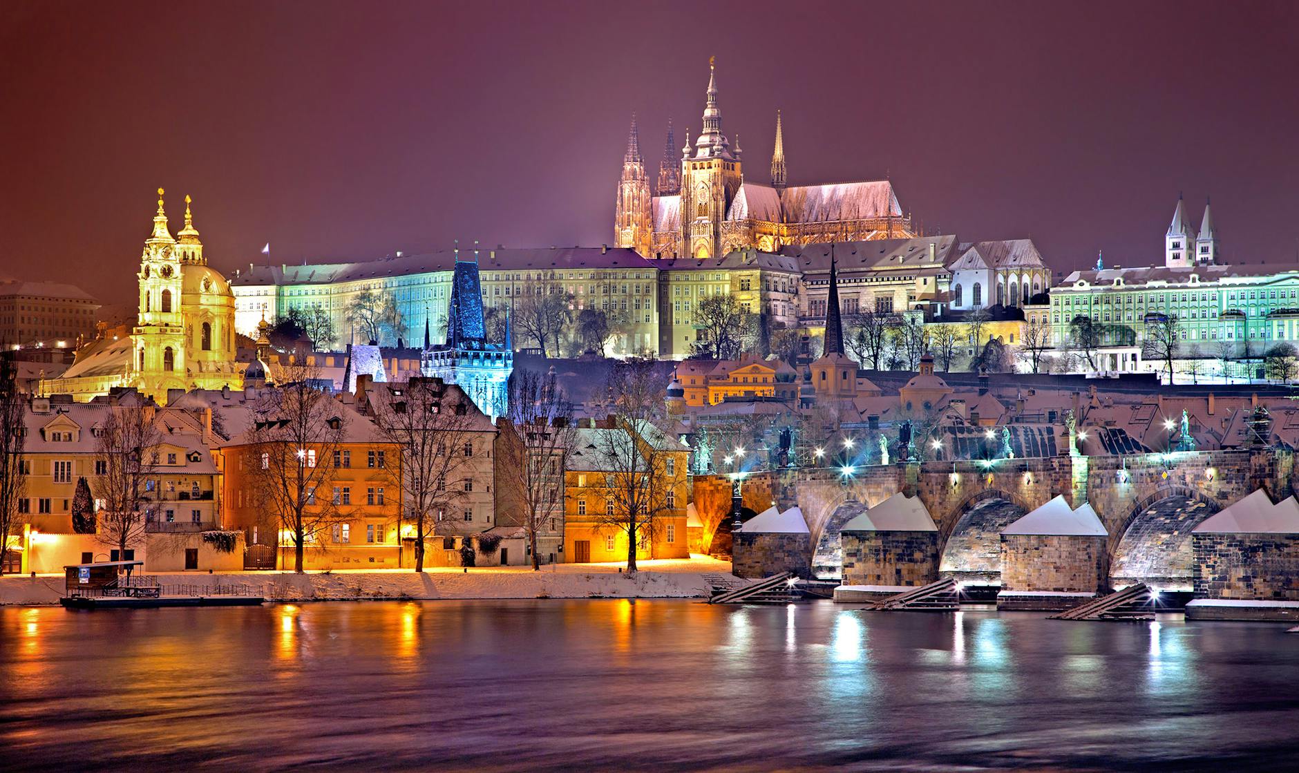 A stunning night view of Prague Castle and Charles Bridge illuminated, reflecting on the Vltava River, symbolizing the connection and cultural richness between Czech and English-speaking communities.