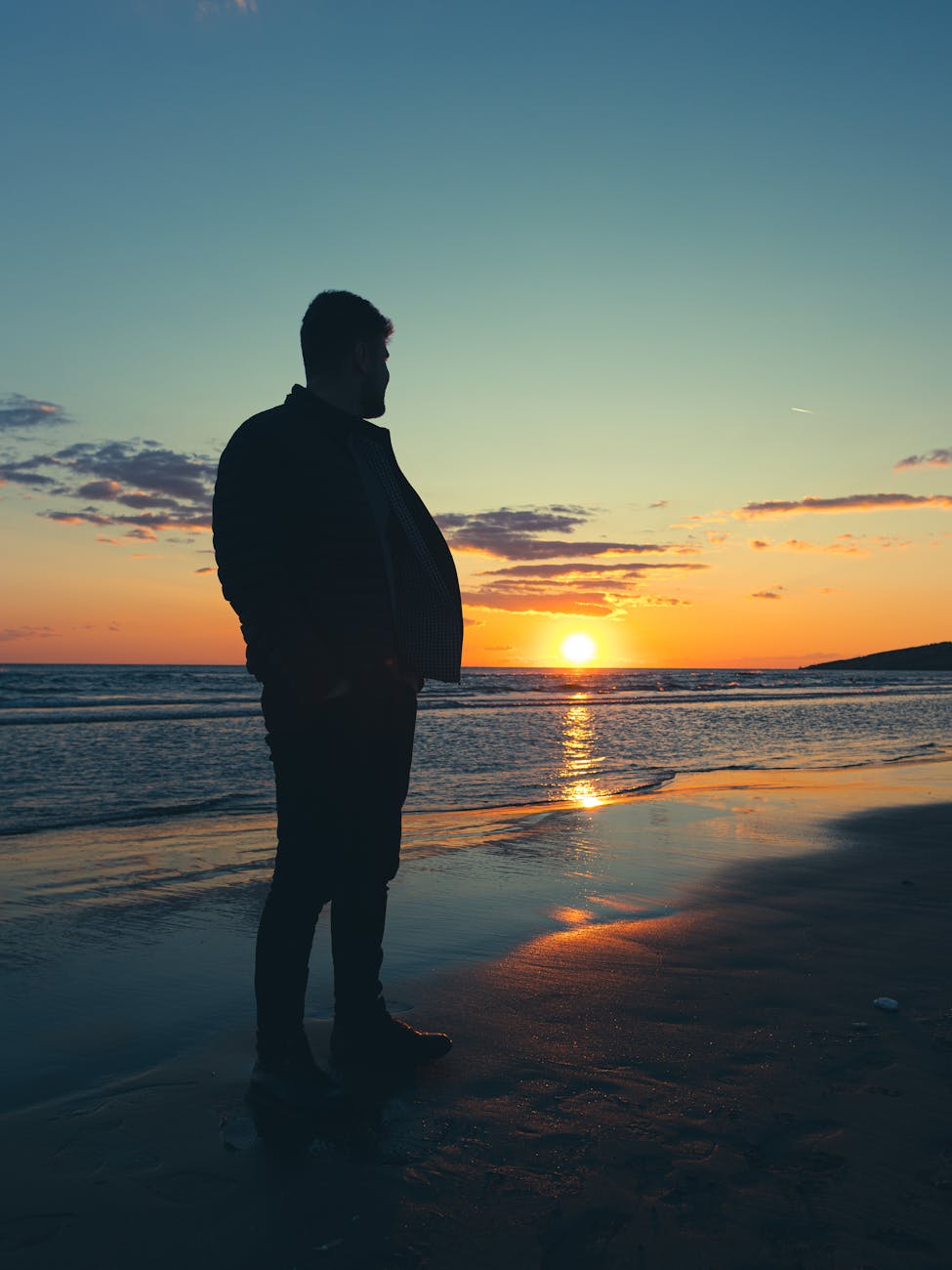 Silhouette of a man standing on a beach during sunset, with the golden sun reflecting on the water, symbolizing the serene and vibrant culture of Aruba.