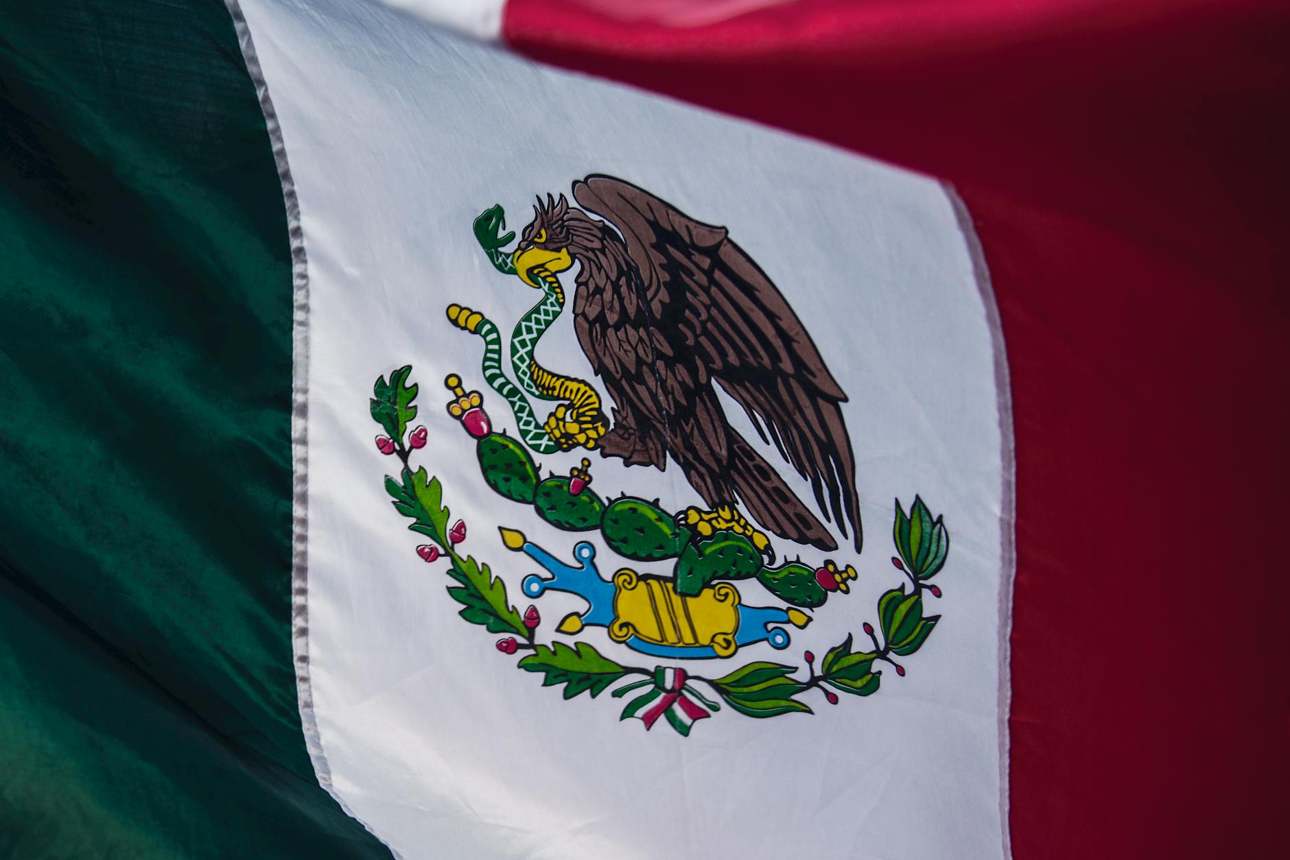 The Mexican flag waving in the wind, featuring an eagle holding a snake in its beak and talon, perched on a cactus, symbolizing Mexico's rich history and cultural heritage.