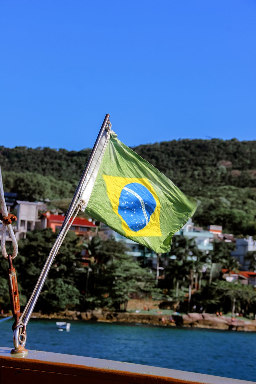 Brazilian flag flying on a sunny day, representing the Portuguese-speaking community in Brazil, with lush greenery and buildings in the background.