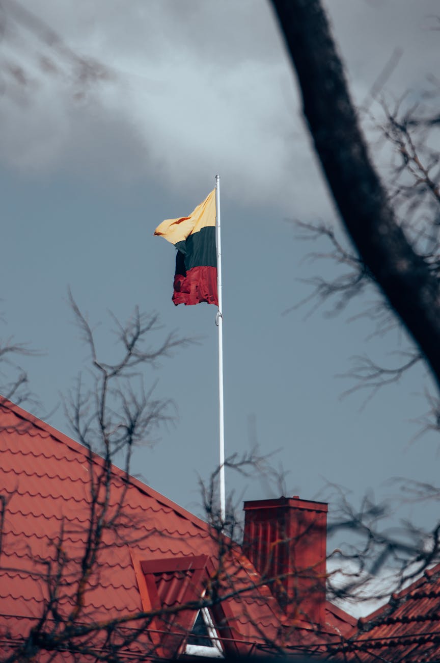The Lithuanian flag waving atop a building with a red roof, symbolizing the nation's pride and resilience.
