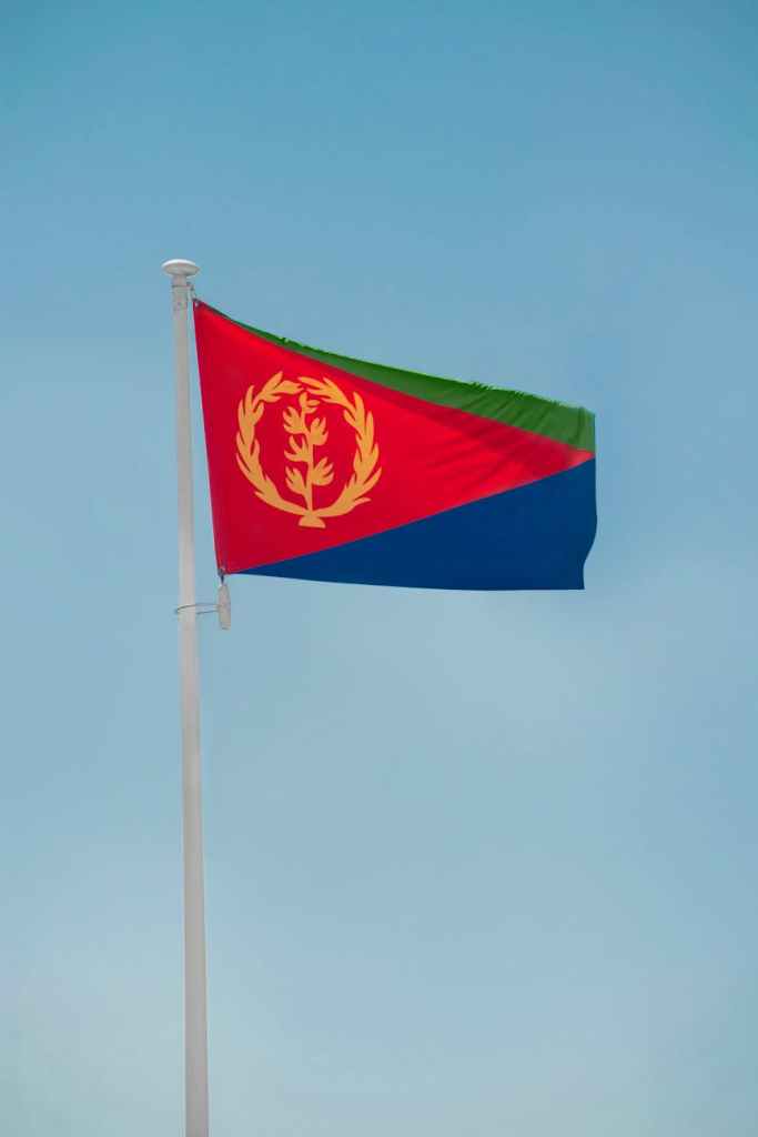 Eritrea flag hanging on a white pole with a clear sky background.