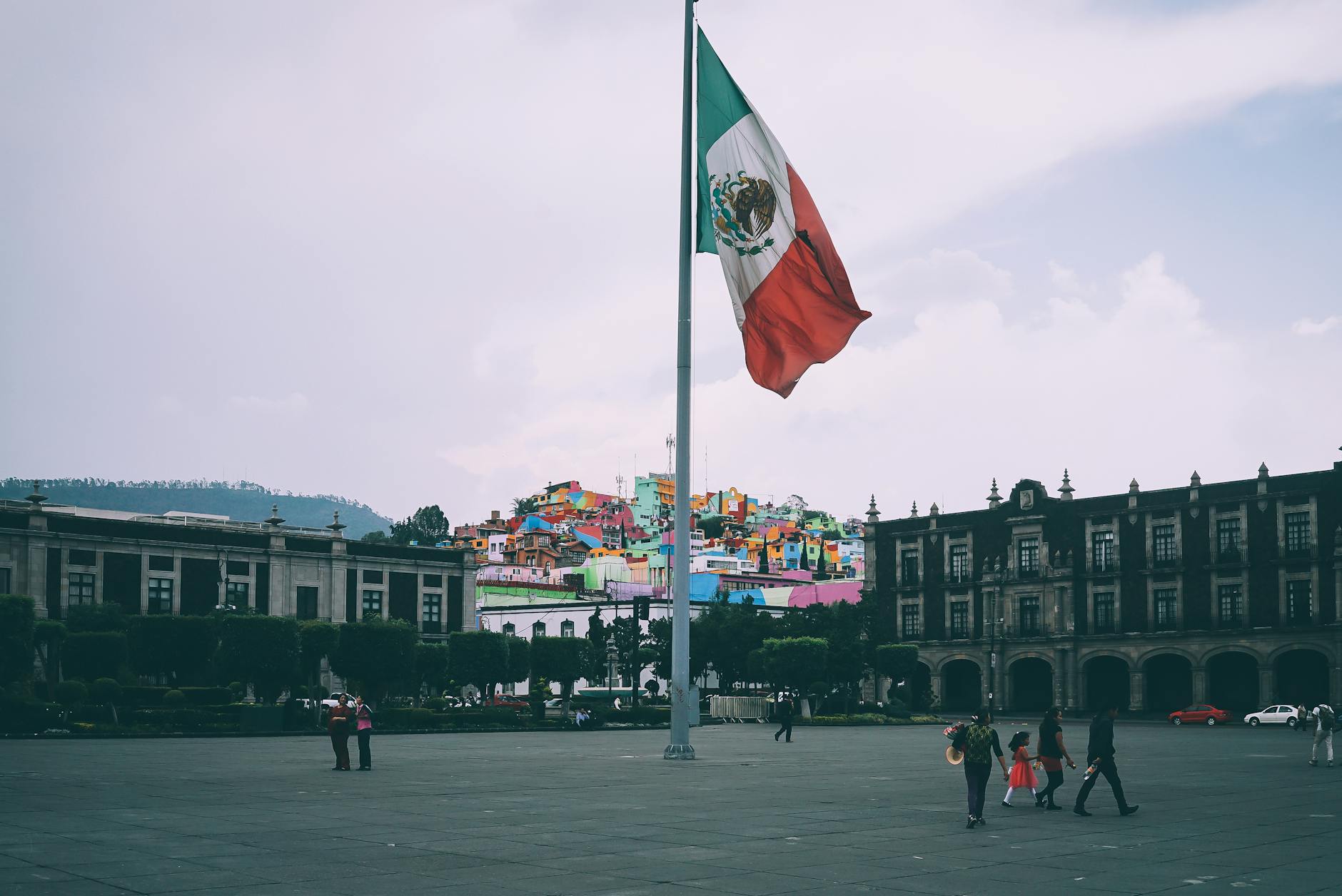 Mexican flag flying in a central plaza with colorful buildings in the background, symbolizing the diverse cultural and linguistic heritage of Mexico.