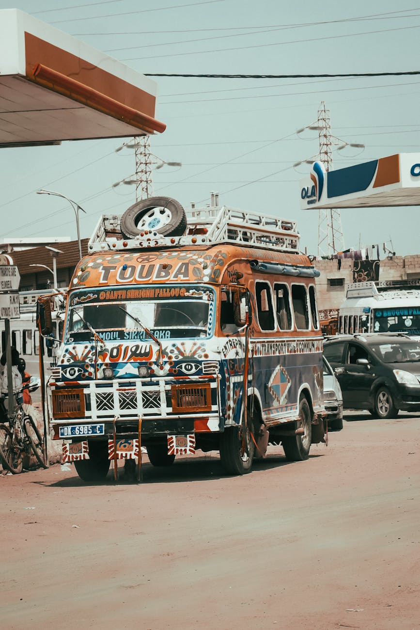 A colorful, traditional Senegalese bus with the word "TOUBA" painted on the front, symbolizing transportation common in Southern Senegal, parked near a fuel station.