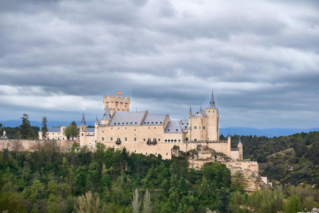 A majestic castle surrounded by lush greenery and under a cloudy sky, with a flag flying atop one of its towers.