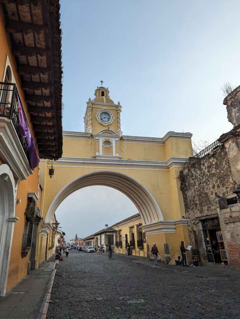 The iconic Santa Catalina Arch in Antigua, Guatemala, with a cobblestone street and colonial architecture, under a clear sky.