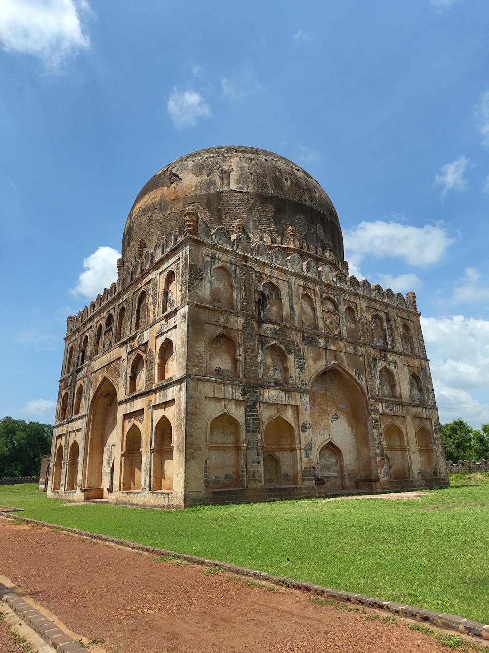 Ancient architectural structure with a large dome and intricate stonework set against a clear blue sky in Karnataka, India.