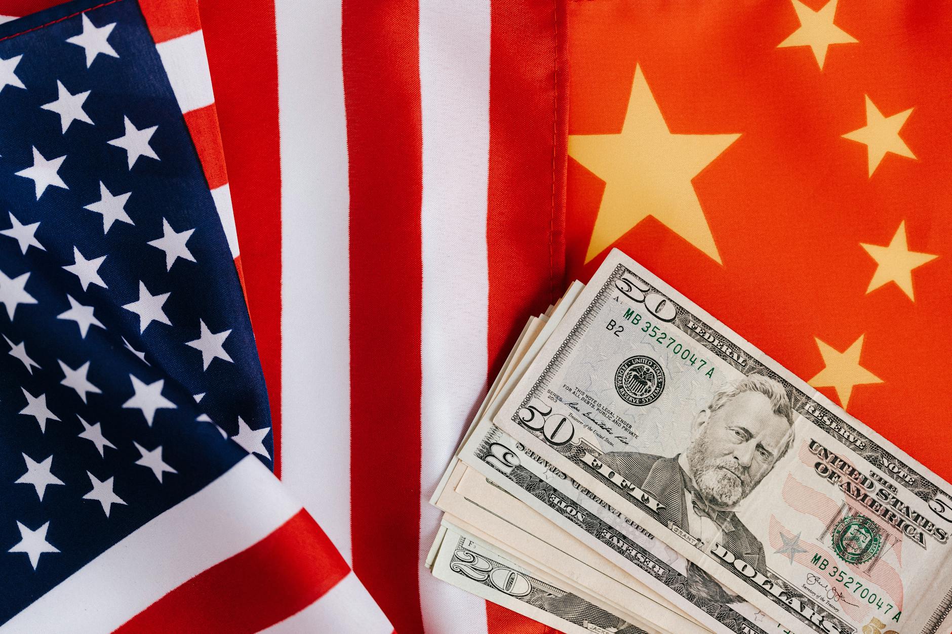 American and Chinese flags side by side with a stack of US dollar bills, symbolizing cultural and economic connections.