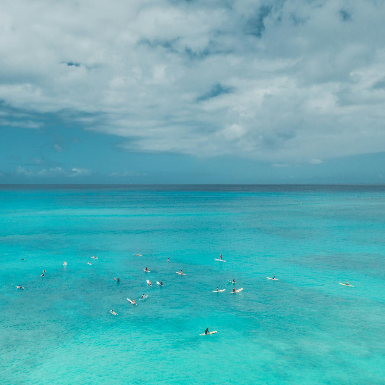 A group of people paddleboarding on a serene turquoise ocean under a partly cloudy sky.