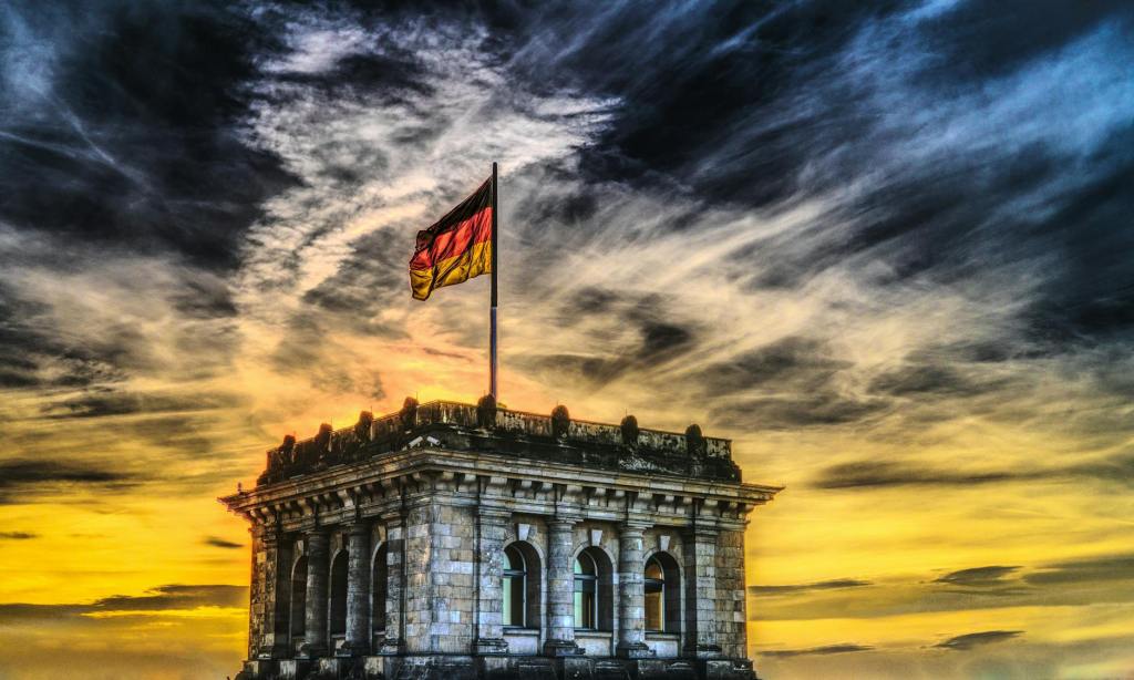 A building with an ornate facade and the German flag flying atop, set against a dramatic sunset sky.
