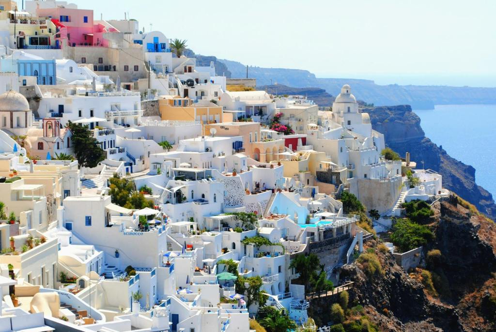 Whitewashed buildings perched on a cliffside overlooking the blue sea in Santorini, Greece, under a clear sky.